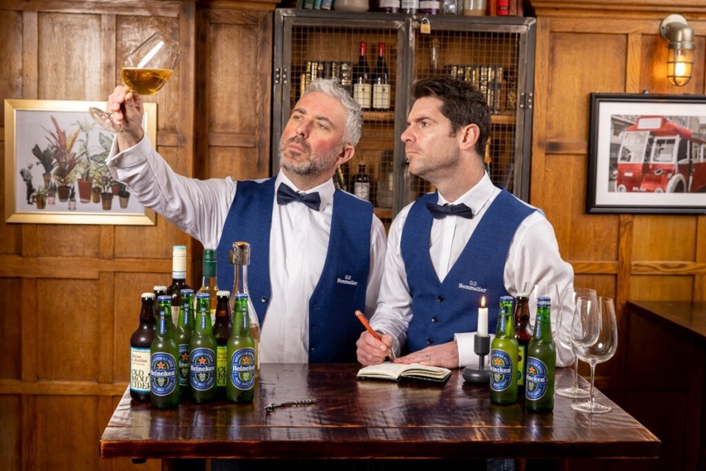 Two bar men looking at a glass with Heineken alcohol beer in front of them