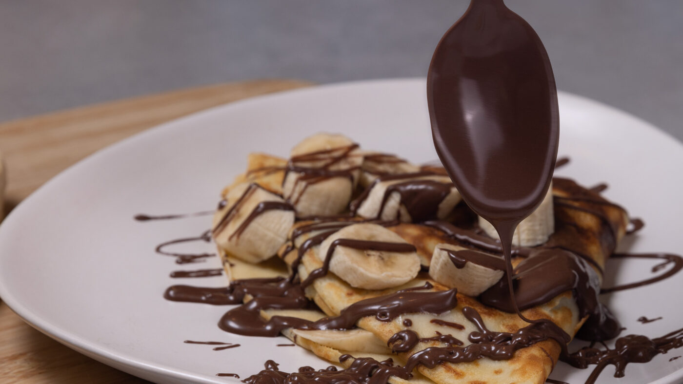 Close up image of chocolate being drizzled over a stack of pancakes
