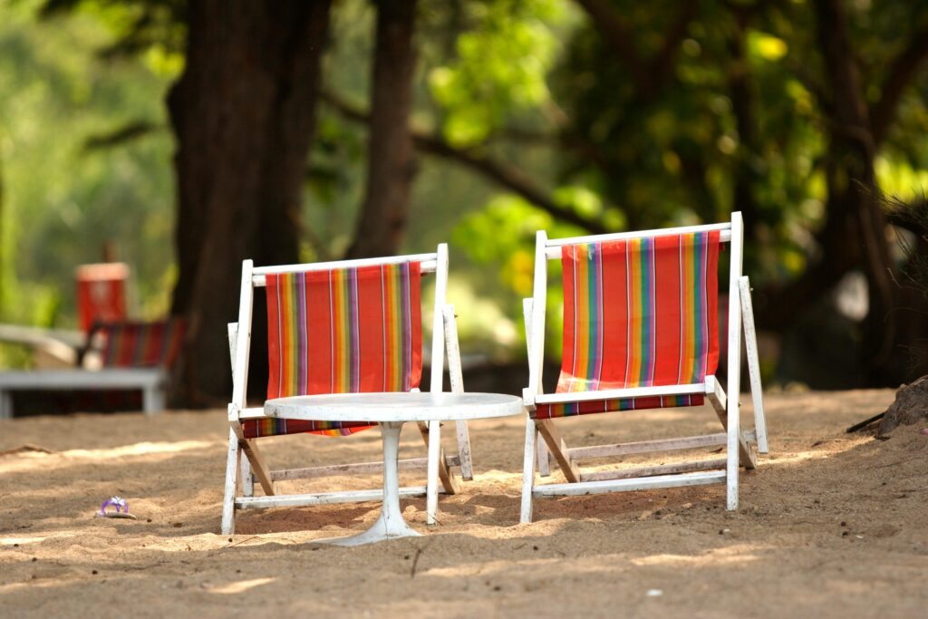 Two stripy deck chairs under some green trees on a sunny day