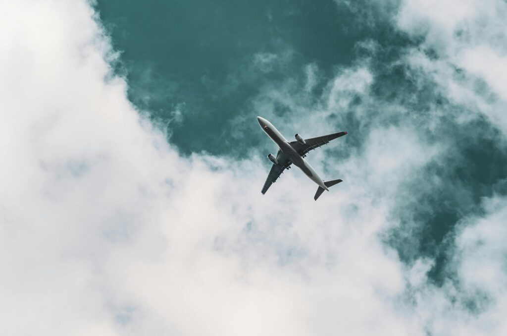 A plane from below high in the blue sky with white clouds behind