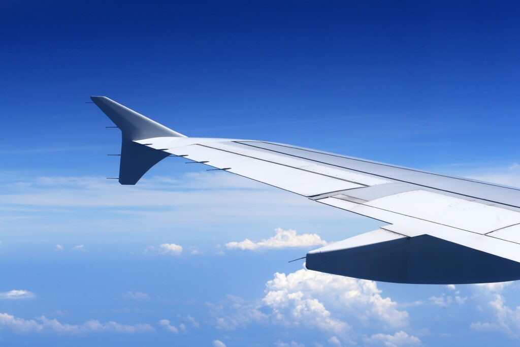 The wing of a plane with blue sky and clouds in the background