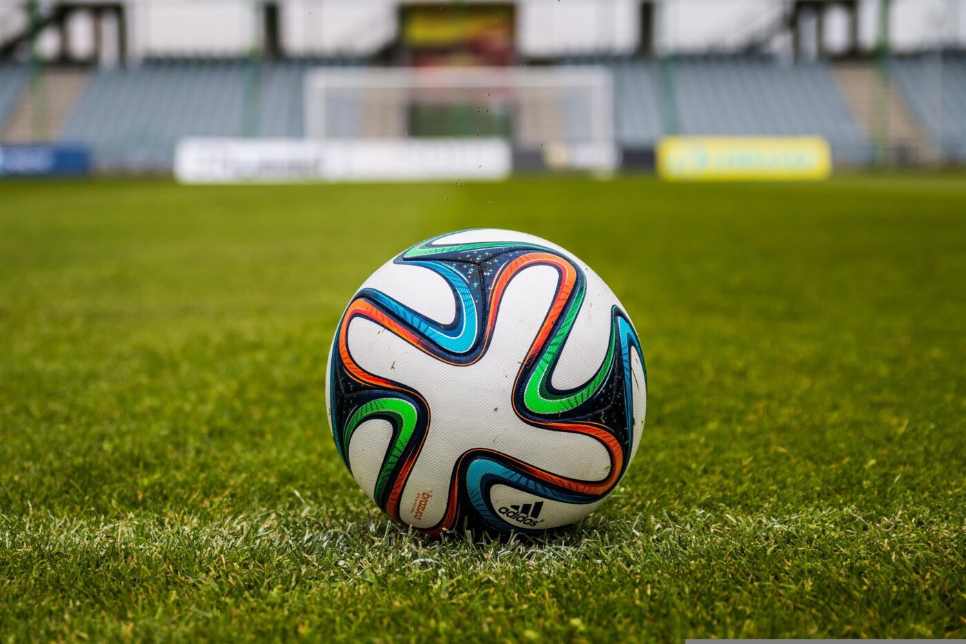 A football with red green blue and black patterns on a green grass pitch