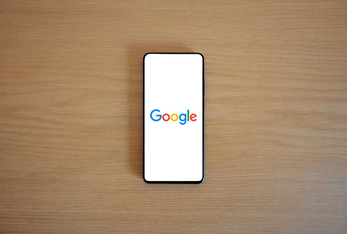A phone on a wooden table with the Google logo on