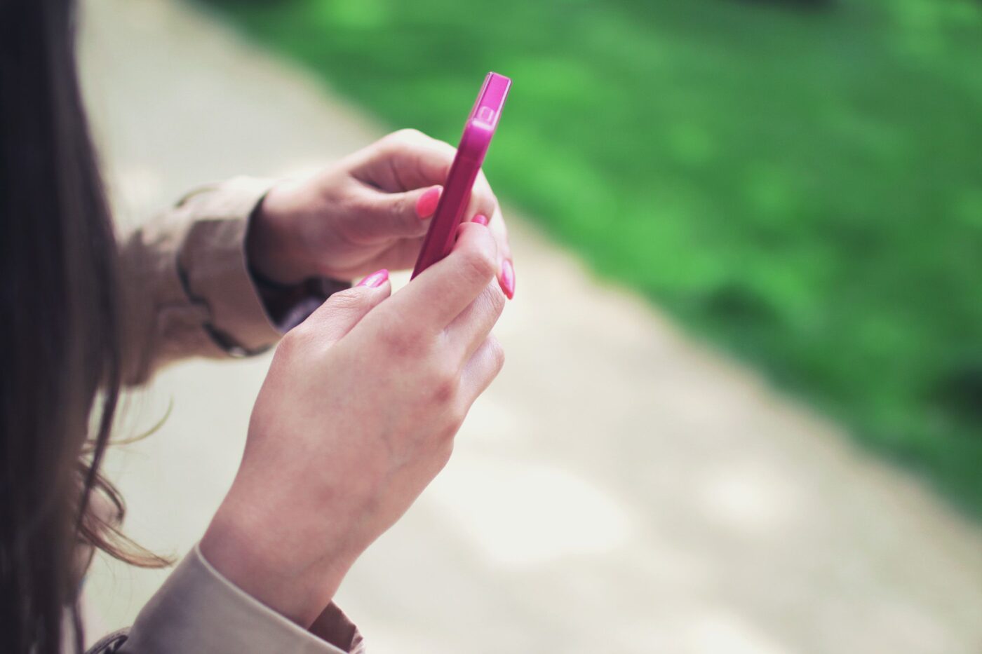 Young person holds a pink phone with green grass in the background
